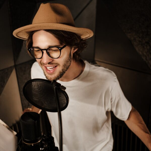 Attractive stylish male musician singing in microphone recording song in professional studio