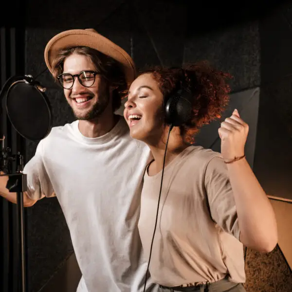 Young attractive musicians happily singing together recording new song in modern sound studio